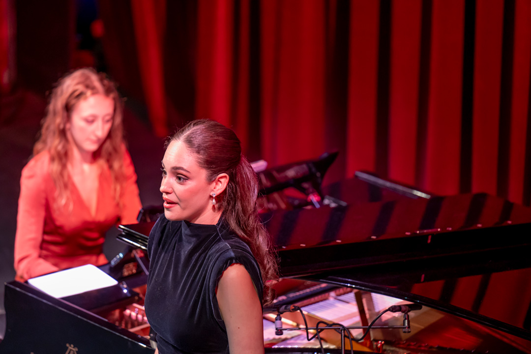 A female student singing on stage with piano accompaniment on stage.